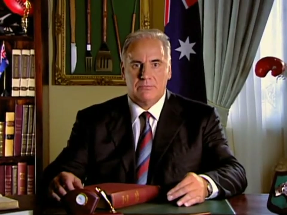 Address to the Nation (2006), scene 3 at 00:45: The camera slowly zooms in on Kekovich's face, increasing the intensity of his address. His expression remains dead serious, adding to the comedic effect of his increasingly absurd list of behaviours.