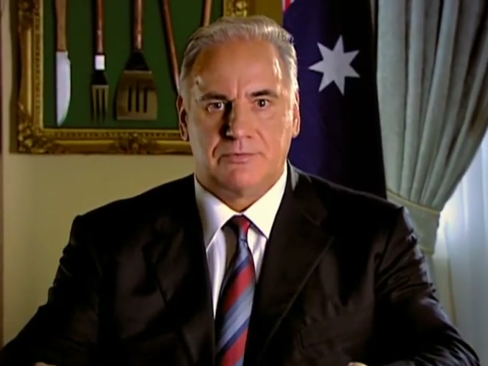 Address to the Nation (2006), scene 4 at 01:12: The close-up on Kekovich is at its tightest. He delivers his final instructions with the conviction of a visionary leader, before breaking into a slight, knowing smile for the first time.