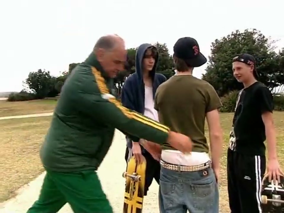 Address to the Nation (Australia Day Party) (2007), scene 3 at 00:37: Kekovich, now in a green and gold Australian tracksuit, walks purposefully with minders. He approaches a group of teenage skateboarders.