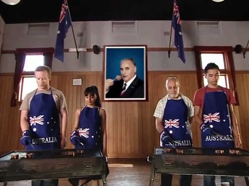 Address to the Nation (Australia Day Party) (2007), scene 5 at 01:39: Kekovich continues his speech. The on-screen text "ADP Australia Day Party" appears with a logo of the Southern Cross morphing into a lamb chop.