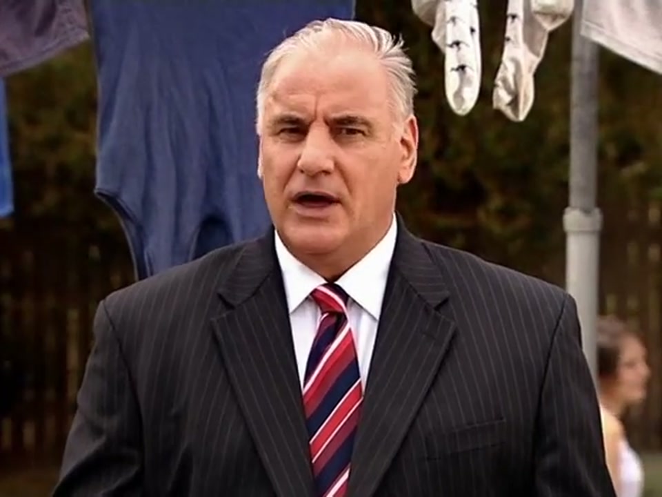 Address to the Nation (Australia Day Party) (2007), scene 6 at 02:36: The speech moves from the formal lectern to a quintessential Australian backyard, with a Hills Hoist clothesline and a barbecue. People are playing backyard cricket in the background.