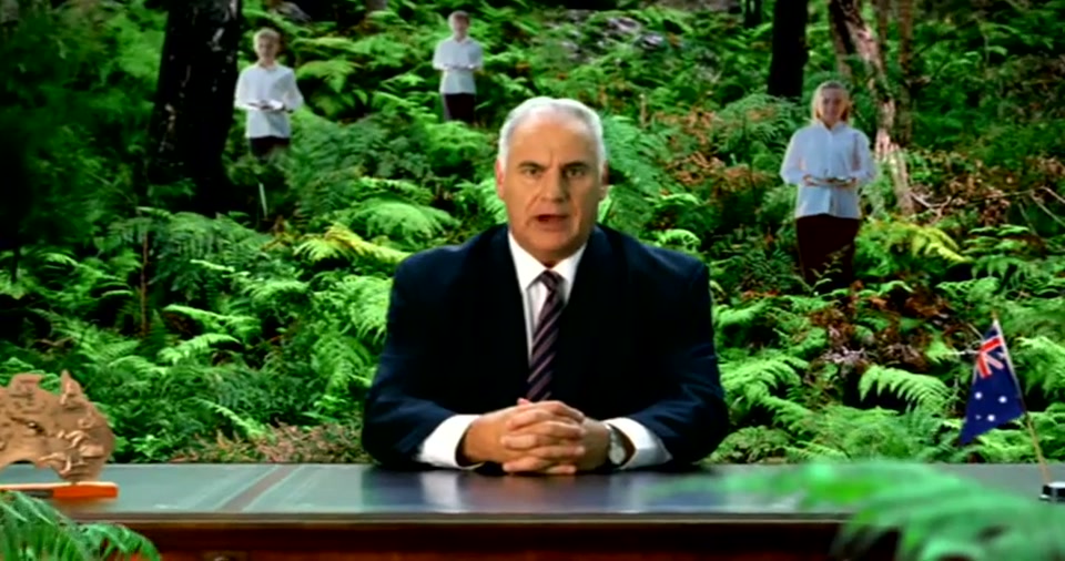 Australia Day Address (2008), scene 3 at 00:44: The setting changes again to a lush, green fern gully or rainforest. The lighting is darker and cooler. The "waiters" are still present, scattered among the ferns.