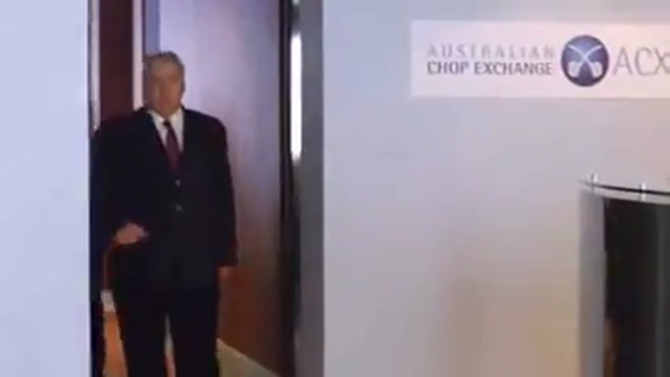 Address to the Nation (GFC Rally) (2009), scene 2 at 00:28: The camera pulls back to reveal the speaker's desk is fronted by a scrolling red-light stock ticker. An Australian flag sits on the desk.