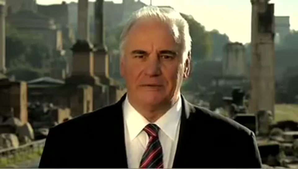 Address to the United Nations of Australia (2011), scene 1 at 00:06: The ad opens on Sam Kekovich, dressed in a dark suit and tie, standing in the middle of the Roman Forum. The lighting is dramatic, suggesting an important historical moment.