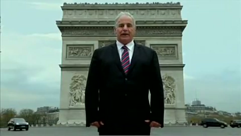 Address to the United Nations of Australia (2011), scene 2 at 00:20: Kekovich stands in a snow-covered English cricket ground, a traditional pavilion in the background. He holds an inflatable cricket bat.