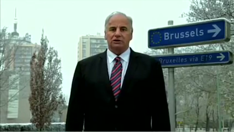 Address to the United Nations of Australia (2011), scene 3 at 00:26: Kekovich stands on a snowy street with a sign pointing towards "Brussels." He then appears in front of the Eiffel Tower, holding up a tiny pair of cooked frog's legs.