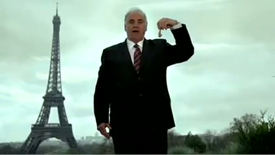 Address to the United Nations of Australia (2011), scene 3 at 00:30: Kekovich stands on a snowy street with a sign pointing towards "Brussels." He then appears in front of the Eiffel Tower, holding up a tiny pair of cooked frog's legs.