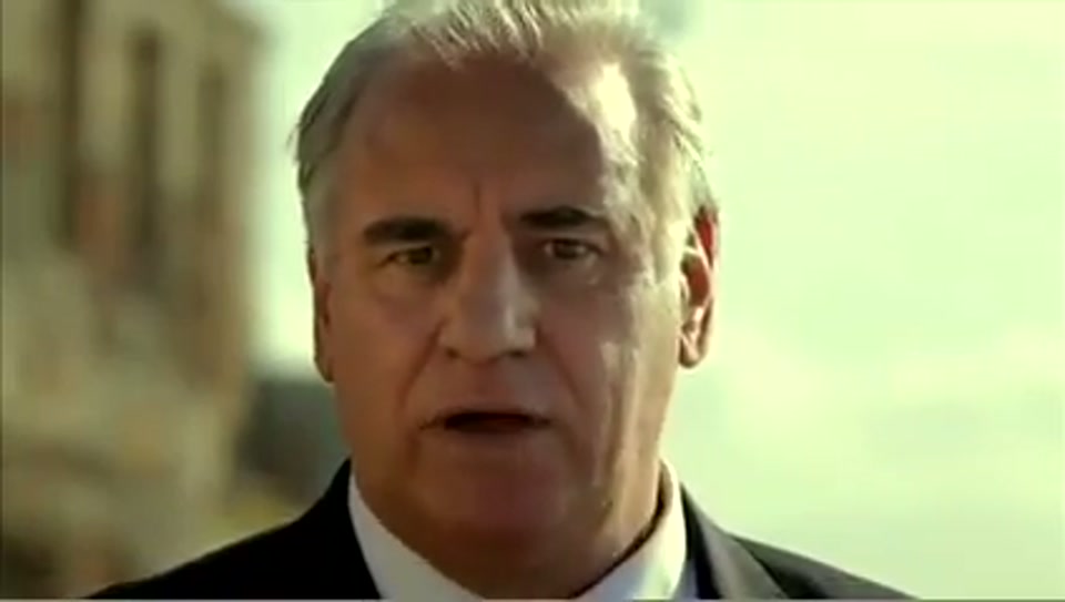 Address to the United Nations of Australia (2011), scene 4 at 00:47: Kekovich stands before the Acropolis in Athens. The shot cuts to an extreme close-up of his face, then to a visual joke where he is seen riding a donkey along a beach, led by a local man.