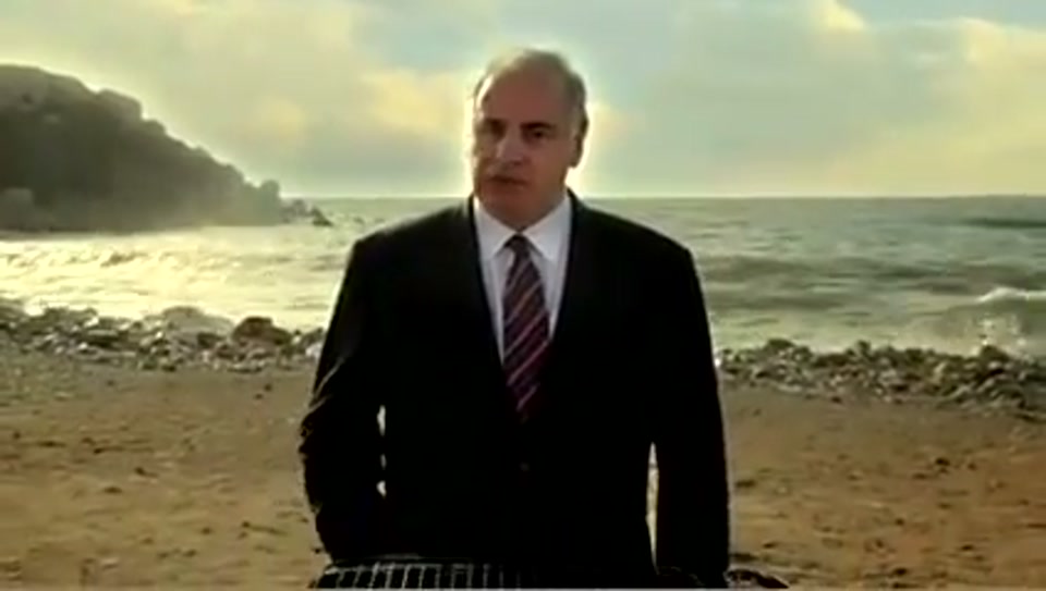 Address to the United Nations of Australia (2011), scene 6 at 01:12: Kekovich stands on a dramatic, windswept beach. A barbecue grill (a Weber kettle) is set alight on the beach.