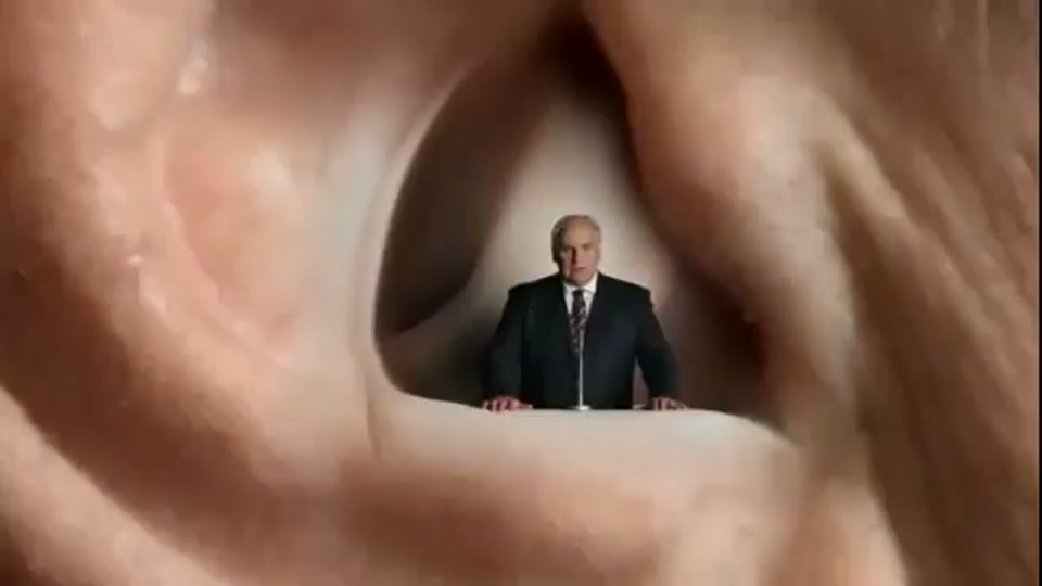 Lambnesia (2013), scene 7 at 01:13: Kekovich walks out of a glowing doorway into a dark, smoky space. The camera follows him as he walks towards it, eventually moving through a giant ear canal. He is seen miniaturised, standing at a lectern inside the ear.
