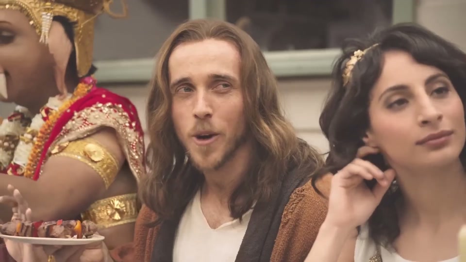 Gods (You Never Lamb Alone) (2017), scene 1 at 00:06: The scene opens on a long dinner table in a brightly lit backyard patio. A man dressed as the Greek god Zeus, with a white beard, toga, and golden laurel wreath, is speaking to a man dressed as Jesus.