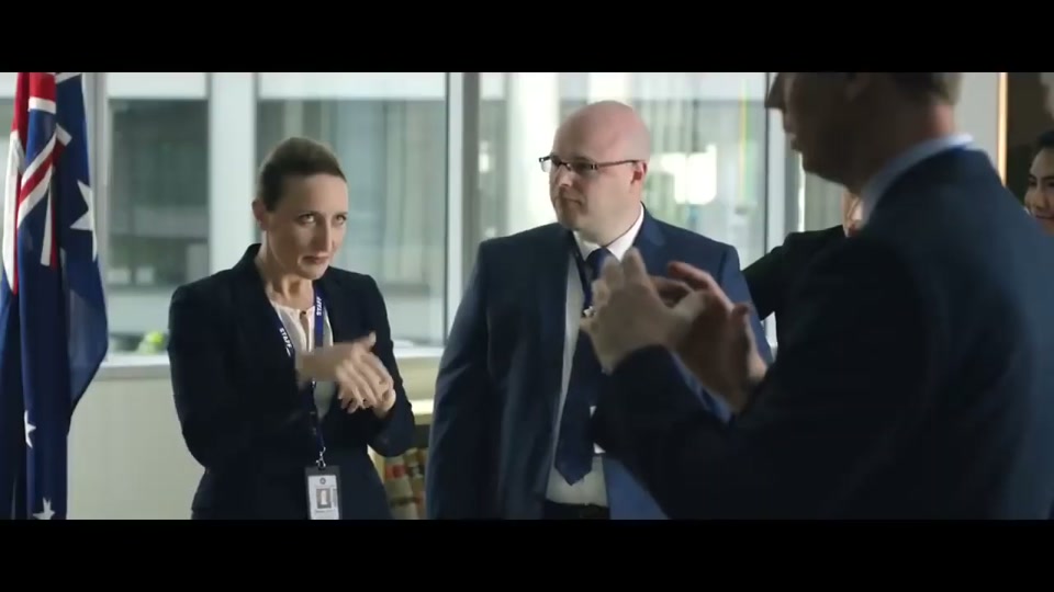Unite Australia and New Zealand (2019), scene 2 at 00:29: The scene abruptly cuts to a bright, sterile, modern government office. A group of bureaucrats in contemporary suits stand around a table with a similar map. The lead bureaucrat, "Gary," laments Australia's state.