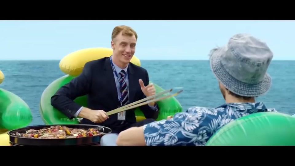 Unite Australia and New Zealand (2019), scene 3 at 00:59: The scene shifts to the open ocean. A small charcoal barbecue on an orange inflatable ring floats on the water, sizzling with lamb chops and skewers.