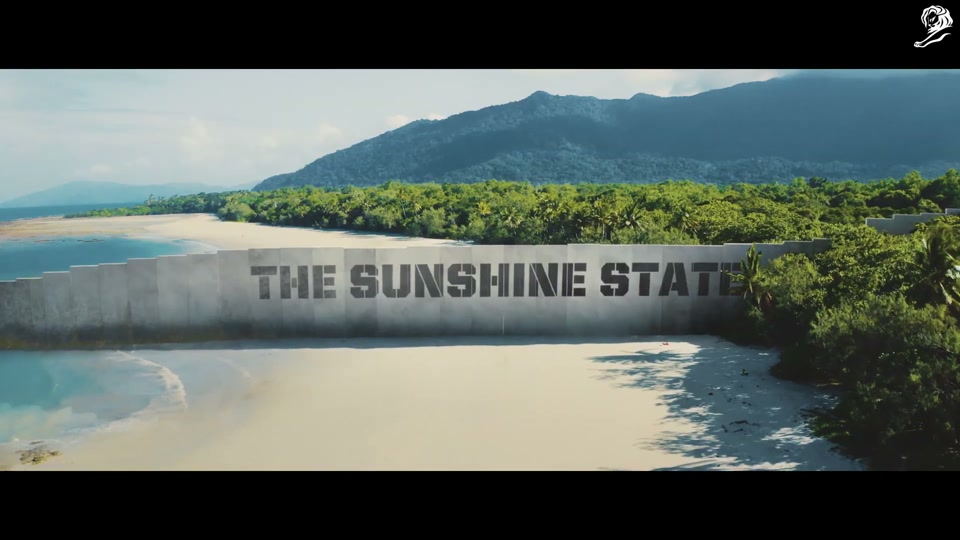 Make Lamb Not Walls (2021), scene 1 at 00:13: The ad opens with a man on a ladder using a paint roller to apply black paint to a colossal concrete wall that stretches to the horizon. The on-screen text "NEW SOUTH WALL" is stencilled onto it.