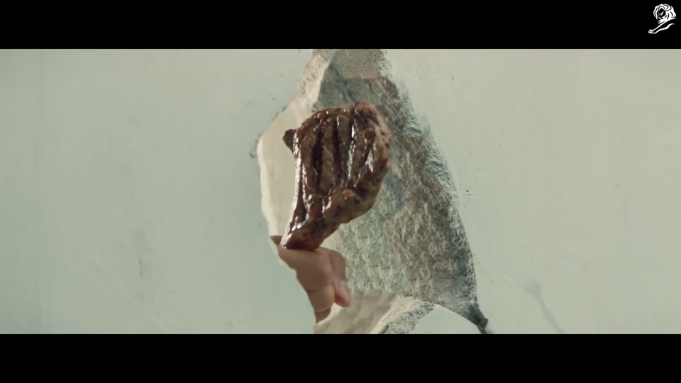 Make Lamb Not Walls (2021), scene 2 at 01:00: An elderly man, carrying grocery bags, walks along the wall. He stops and sniffs the air, intrigued. He discovers a small hole in the concrete. He kneels down to peer through it.
