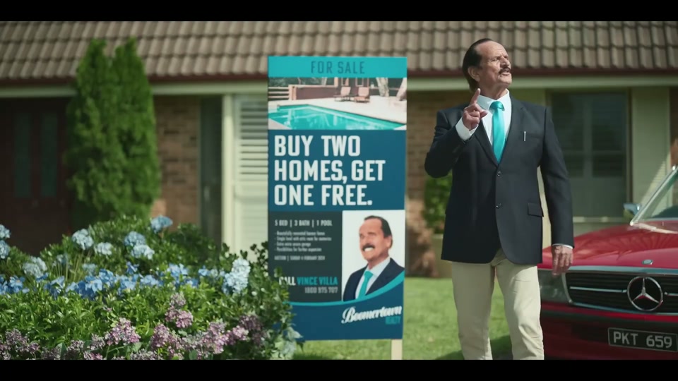 The Generation Gap (2024), scene 1 at 00:18: The scene opens in a quiet, manicured Australian suburb called "Boomertown." An elderly man on a bicycle, wearing a helmet, does a paper round. He throws a newspaper onto a perfect green lawn.