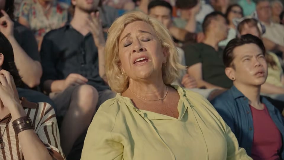 The Comments Section (2025), scene 3 at 00:44: The groomers look up at the sky, concerned. The scene shifts to an aerial shot of a wind turbine on a rolling green hill by the sea. The entire stadium grandstand is now superimposed on the hill.