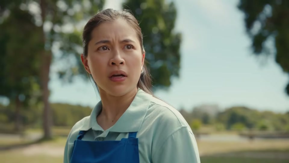 The Comments Section (2025), scene 3 at 00:37: The groomers look up at the sky, concerned. The scene shifts to an aerial shot of a wind turbine on a rolling green hill by the sea. The entire stadium grandstand is now superimposed on the hill.