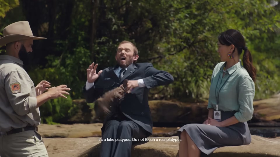 Happiness Index (2026), scene 4 at 01:17: The group is now in the back of the car, driving through a city. They then drive through a lush, green forest. Next, they are by a creek, where a park ranger is showing a male auditor a platypus.