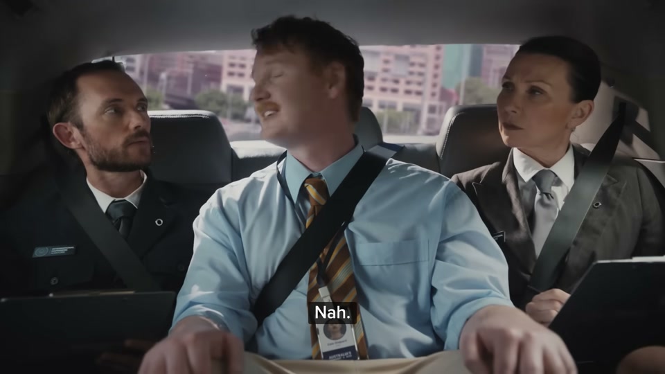 Happiness Index (2026), scene 4 at 01:07: The group is now in the back of the car, driving through a city. They then drive through a lush, green forest. Next, they are by a creek, where a park ranger is showing a male auditor a platypus.