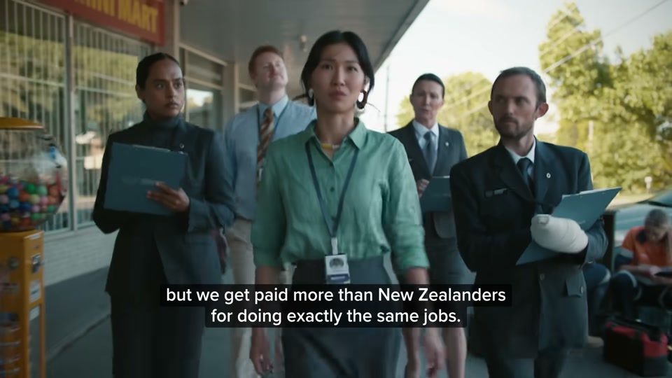 Happiness Index (2026), scene 5 at 01:58: A rapid montage of Australian cultural scenes: - A classroom where an Indigenous elder is speaking. - The auditors in a car in a suburban setting.